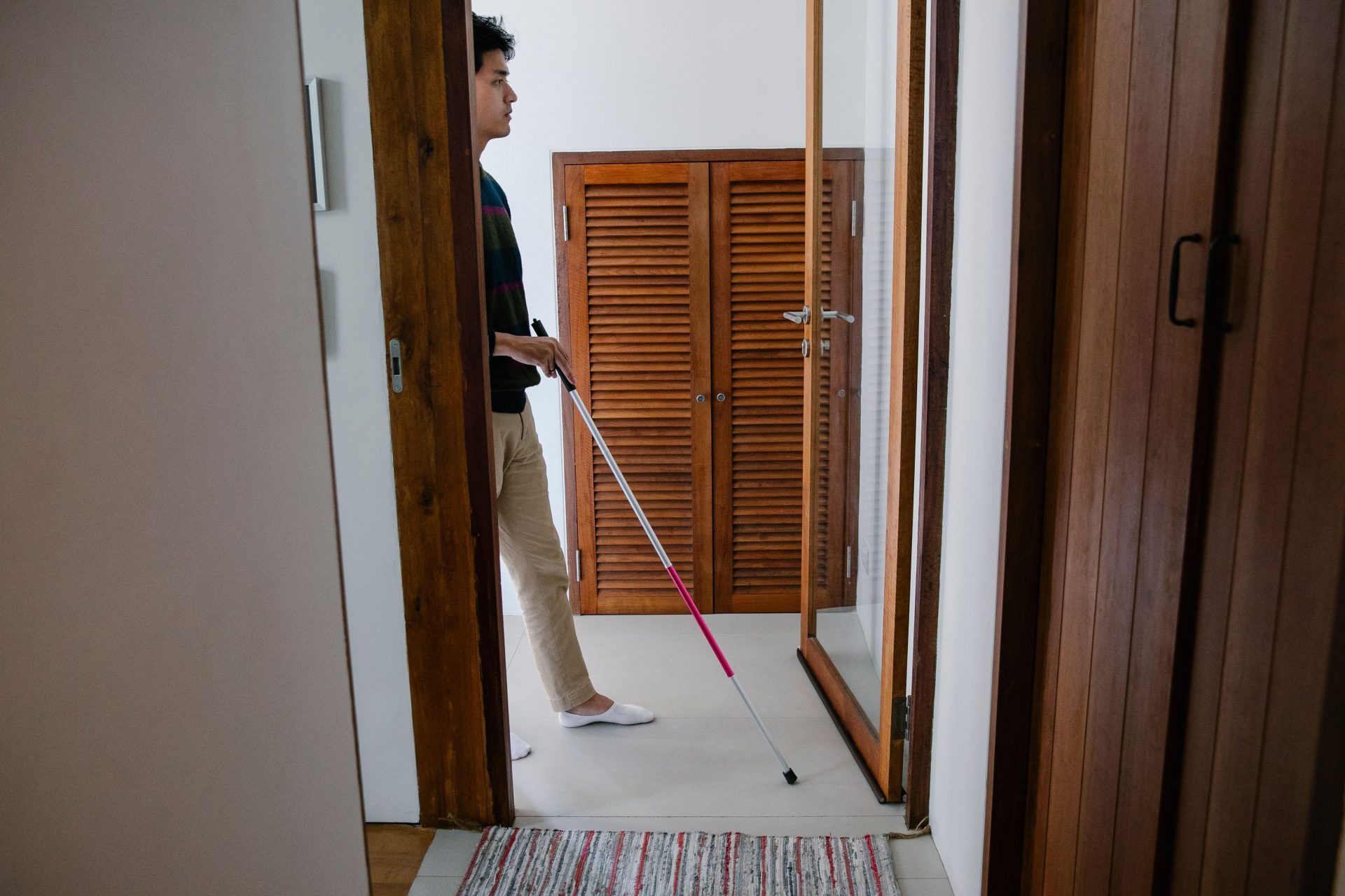 Man using a walking stick for navigation indoors, emphasizing independence and visual impairment.