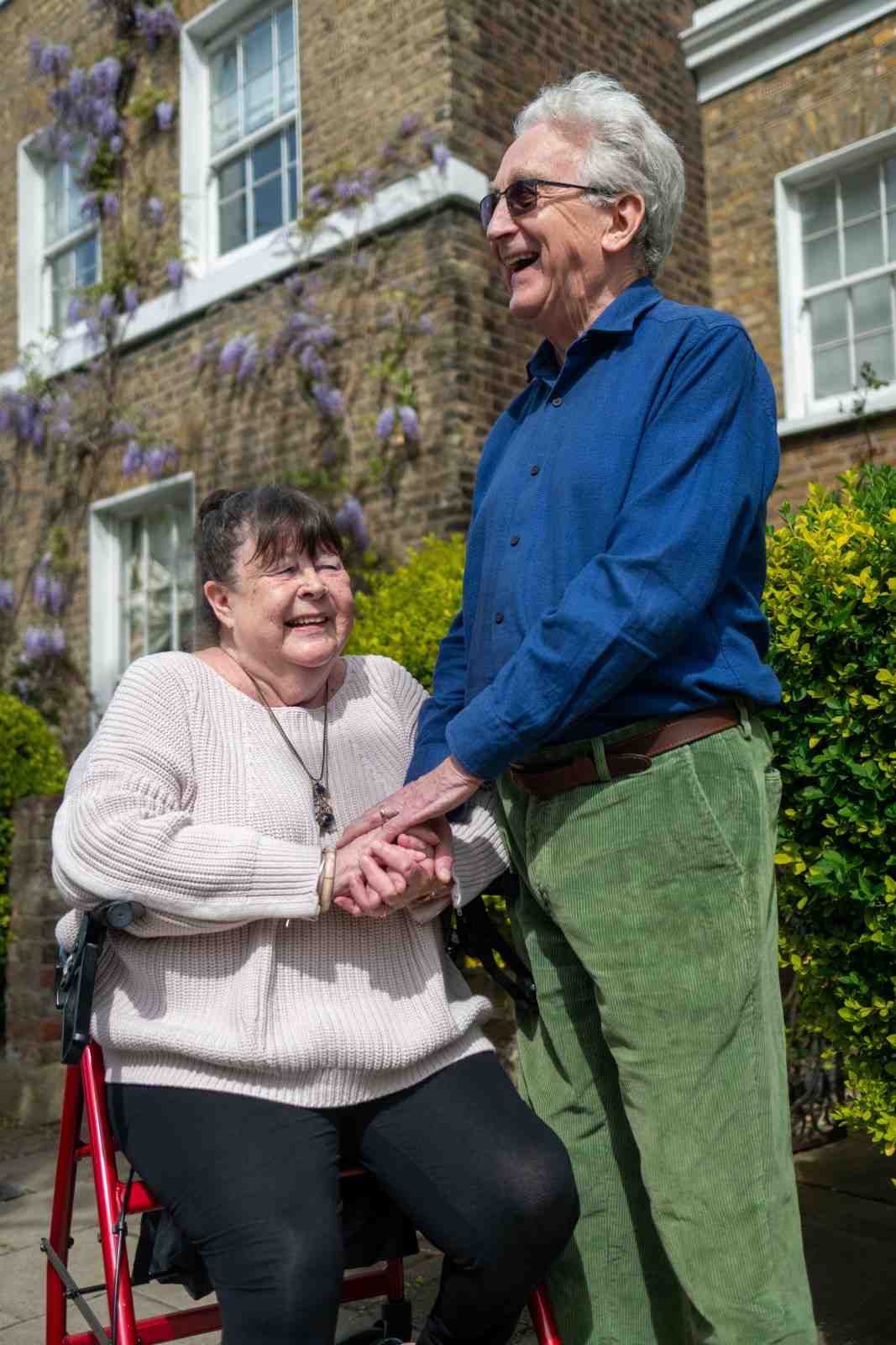 Happy senior couple holding hands outside a building under sunny skies.
